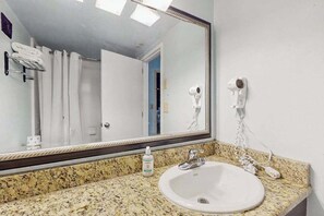 Ein Badezimmer mit einer Granit-Arbeitsplatte, einem weißen Waschbecken, einem Spiegel und einem an der Wand befestigten Föhn.
