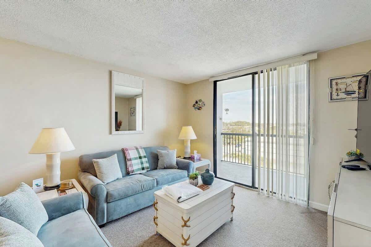 Sala de estar con sofá, mesa de centro y lámpara. Hay un ventanal corredero que da a un balcón.