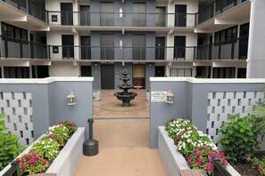 Ein mehrstöckiges Gebäude mit einem zentralen Innenhof, einer Fontäne und Blumenbeeten.