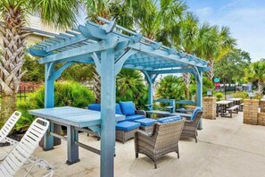 Ein Patio im Freien mit einer blauen Pergola, Sitzgelegenheiten und einer Ziegelwand.