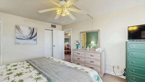 A bedroom with a bed, a dresser, a television, and a ceiling fan. - Holiday Towers Unit 607 (Myrtle Beach)
