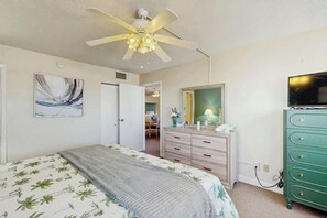 Ein Schlafzimmer mit einem Bett, einem Schminktisch, einem Fernseher und einem Deckenventilator.
