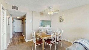 A dining area with a table and chairs, a ceiling fan, and a kitchen area in the background. - Holiday Towers Unit 607 (Myrtle Beach)