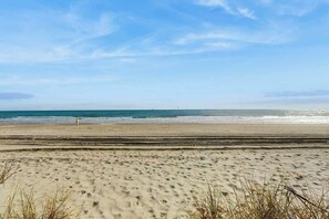 Ein Strand mit blauem Himmel, sandigem Ufer und einer Person, die spazieren geht.
