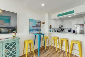 A modern kitchen with white cabinets, a stainless steel refrigerator, and a blue island. - Windsong Unit 303 Condo (North Myrtle Beach)