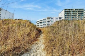 Un chemin menant à un bâtiment situé en bord de mer, doté de plusieurs balcons.