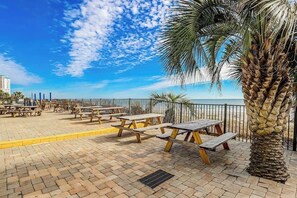 An outdoor seating area with picnic tables and a palm tree, overlooking a body of water. - Bluewater Resort 1006 (Myrtle Beach)