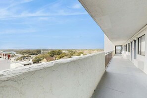 A long, narrow balcony with a concrete wall on one side and a row of windows on the other. - Bluewater Resort 1006 (Myrtle Beach)