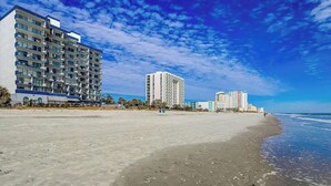 Um hotel na praia com vários andares, uma praia de areia e um céu claro.