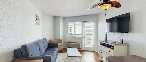 A compact living space with a sofa, a small table, a TV mounted on the wall, and a ceiling fan.