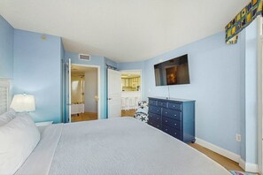 A bedroom with a bed, a dresser, a television, and a bathroom visible through an open door. - Bay Watch Resort 0302 (North Myrtle Beach)