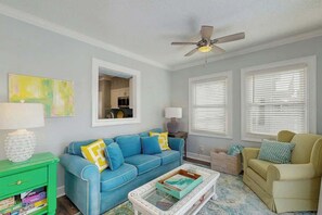 A living room with a blue sofa, a green side table, a white coffee table, and a ceiling fan. - Ward's Landing Retreat (North Myrtle Beach)