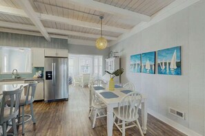 A modern kitchen with white cabinetry, stainless steel appliances, and a dining area with a white table and chairs. - Ward's Landing Retreat (North Myrtle Beach)
