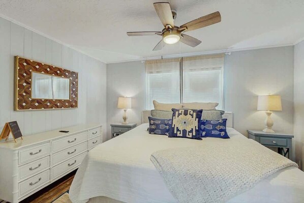 A bedroom with a bed, nightstands, a ceiling fan, a wall-mounted mirror, and a dresser. - Ward's Landing Retreat (North Myrtle Beach)