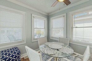 A dining area with a glass table surrounded by white chairs, large windows with blinds, and a ceiling fan. - Ward's Landing Retreat (North Myrtle Beach)