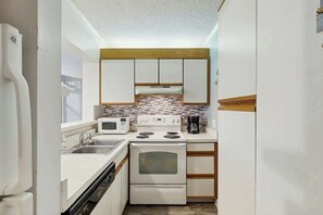 A compact kitchen with white cabinetry, a microwave, stove, and a coffee maker. - Ocean Creek Unit 2424 (Myrtle Beach)