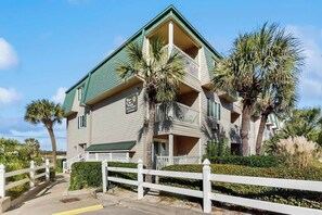 A two-story building with a balcony, surrounded by a white fence and palm trees. - Cozy Captains Retreat (North Myrtle Beach)