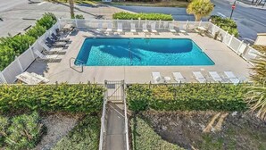 Ein rechteckiger Pool mit einer umlaufenden Sonnenterrasse, Liegestühlen und einem verschlossenen Eingang.