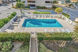 A rectangular swimming pool with a surrounding deck, lounge chairs, and a gated entrance. - Cozy Captains Retreat (North Myrtle Beach)