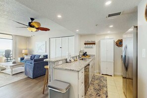 A modern kitchen with a central island, a dining area with a blue sofa, and a ceiling fan. - Verandas Unit 803 Condo (North Myrtle Beach)