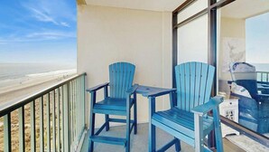 A balcony with two blue Adirondack chairs, a small table, and a view of the beach. - Verandas Unit 803 Condo (North Myrtle Beach)