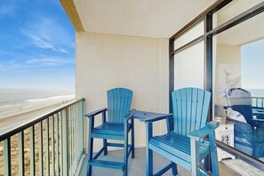 A balcony with two blue Adirondack chairs, a small table, and a view of the beach. - Verandas Unit 803 Condo (North Myrtle Beach)
