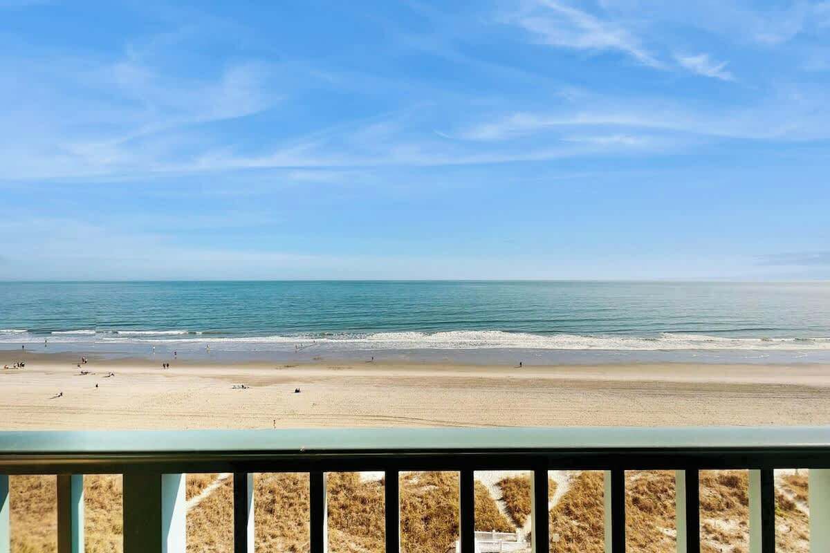 Une vue sur la plage depuis un balcon doté d’une balustrade, avec une plage de sable et l’océan en toile de fond.