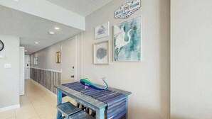 A hallway with a wooden bench, a wall-mounted sink, and framed artwork. - Verandas Unit 803 Condo (North Myrtle Beach)