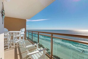 A balcony with white chairs and a glass railing overlooking a beach. - Bahama Sands Unit 1205 (North Myrtle Beach)