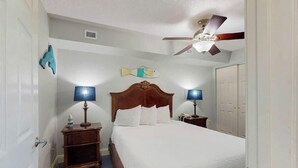Camera d'albergo con un letto singolo, due comodini con lampade, una ventola a soffitto e un decoro raffigurante un pesce al muro.