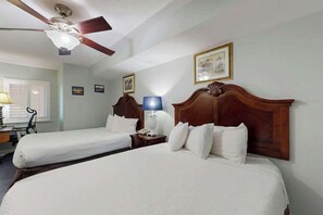 A hotel room with two beds, a ceiling fan, a desk with a lamp, and framed pictures on the wall. - Bahama Sands Unit 1205 (North Myrtle Beach)