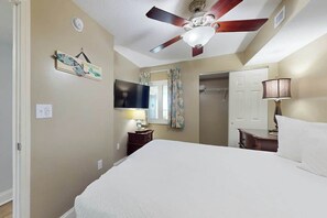 Ein Schlafzimmer mit Bett, Deckenventilator, Fernseher, Nachttisch, Lampe und einer Tür.