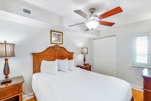 A hotel room with a bed, a nightstand, a lamp, a ceiling fan, a window, and a door. - Bahama Sands Unit 1207 (North Myrtle Beach)