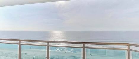 Vista desde un balcón, cielo despejado y mar tranquilo.