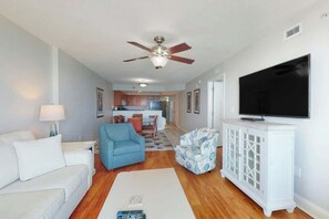 Ein Wohnzimmer mit einer Couch, einem blauen Sessel, einer weißen Kommode mit Fernseher und einem Deckenventilator.