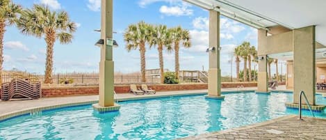 An indoor swimming pool with clear blue water, surrounded by palm trees and lounge chairs.