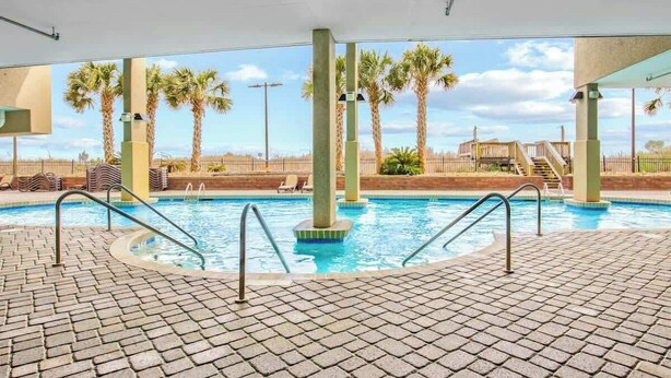 Piscina com deck revestido, palmeiras e área coberta com vista para a paisagem.