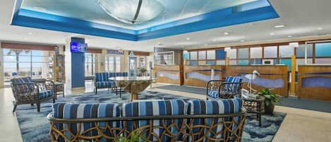 A hotel lobby with a central seating area, a reception desk, and a large window.