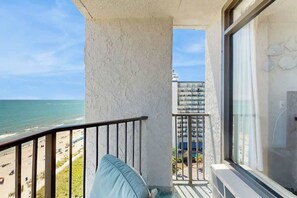 A balcony with a view of the beach and ocean, a white wall, and a window with curtains. - Ocean Park Resort 1222/1224 Combo (Myrtle Beach)
