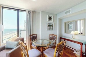 Une pièce comprenant une table ronde en verre, des chaises en osier, un canapé, une console avec une lampe et un grand miroir.