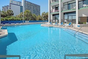 Una piscina limpida con lettini e un edificio sullo sfondo con balconi.