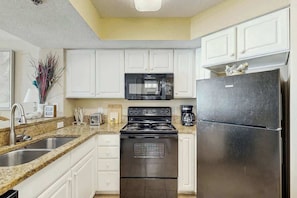 A kitchen with white cabinets, a stainless steel stove, a microwave, and a refrigerator. - Carolinian Beach Resort 0734 (Myrtle Beach)