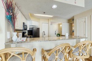A kitchen with white cabinets, a black refrigerator, and a granite countertop. - Carolinian Beach Resort 0734 (Myrtle Beach)