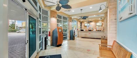A hotel lobby with a reception desk, seating area, and a view of the street outside.