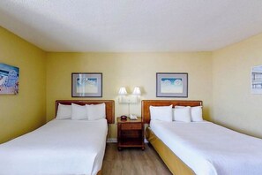 Habitación de hotel con dos camas individuales, una mesita de noche con lámpara y cuadros en las paredes.
