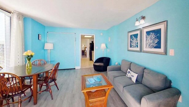 Quarto com uma mesa de jantar, cadeiras, sofá e mesa de centro. Há duas luminárias e quadros nas paredes.