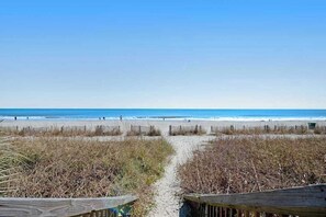 Ein Strandweg, der zum Meer führt, mit blauem Himmel.