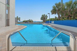 Ein Swimmingpool mit klarem, blauem Wasser, umgeben von einem blauen Zaun, und Palmen im Hintergrund.