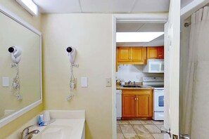 A bathroom with a sink, two hair dryers, and a mirror. Adjacent to the bathroom is a kitchen with wooden cabinets, a microwave, and a stove. - Ocean Park Resort 0322/0324 Combo (Myrtle Beach)