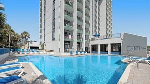 A swimming pool with lounge chairs, a building with balconies, and a clear sky. - Ocean Park Resort 0322/0324 Combo (Myrtle Beach)